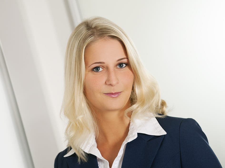 Nadin blickt freundlich in die Kamera. Sie trägt ein weißes Hemd und eine dunkelblaue Jacke.