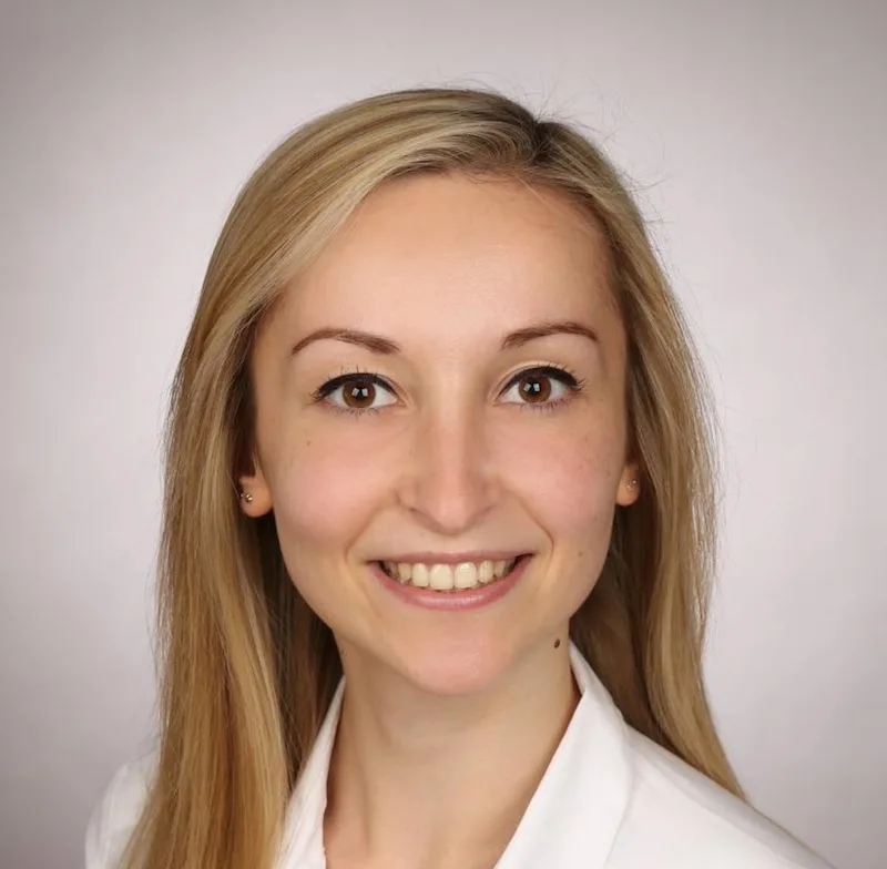 Natalie lächelt in die Kamera. Sie trägt ein weißes Hemd.